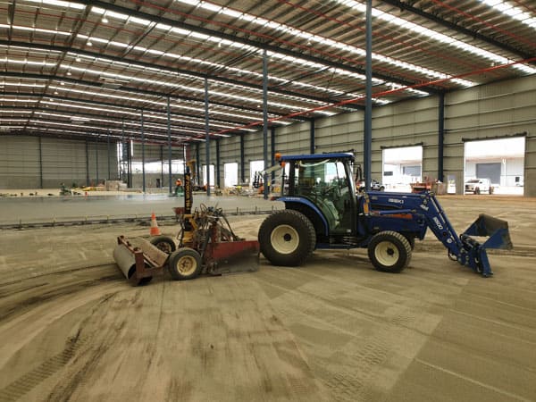 Grader completing ground levelling preparation across a large warehouse.